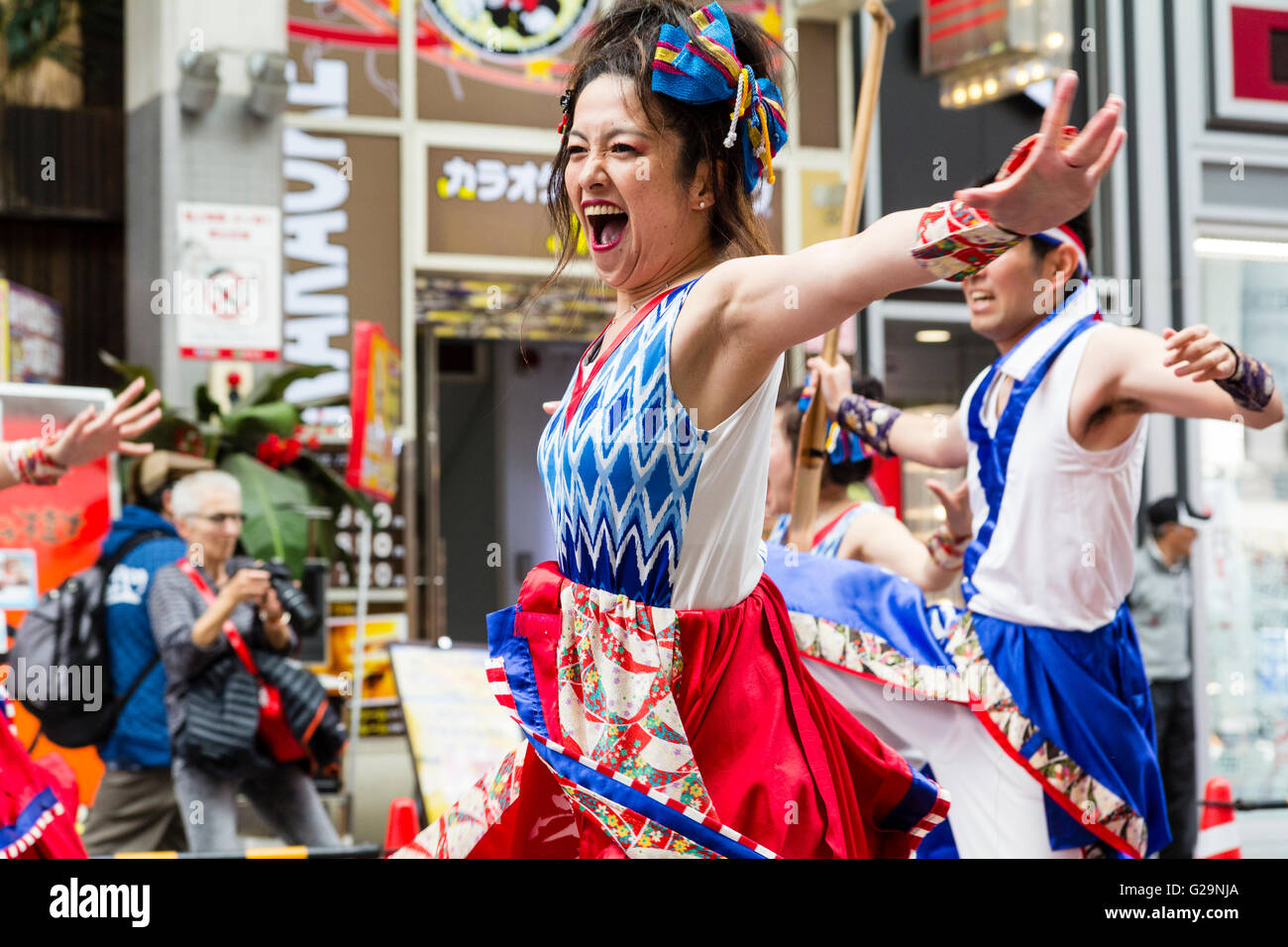 Japan, Kumamoto. Hinokuni Yosakoi dance festival. Close up of Japanese young woman dancer, part of a team, arms outstretched, dancing in mall. Stock Photo