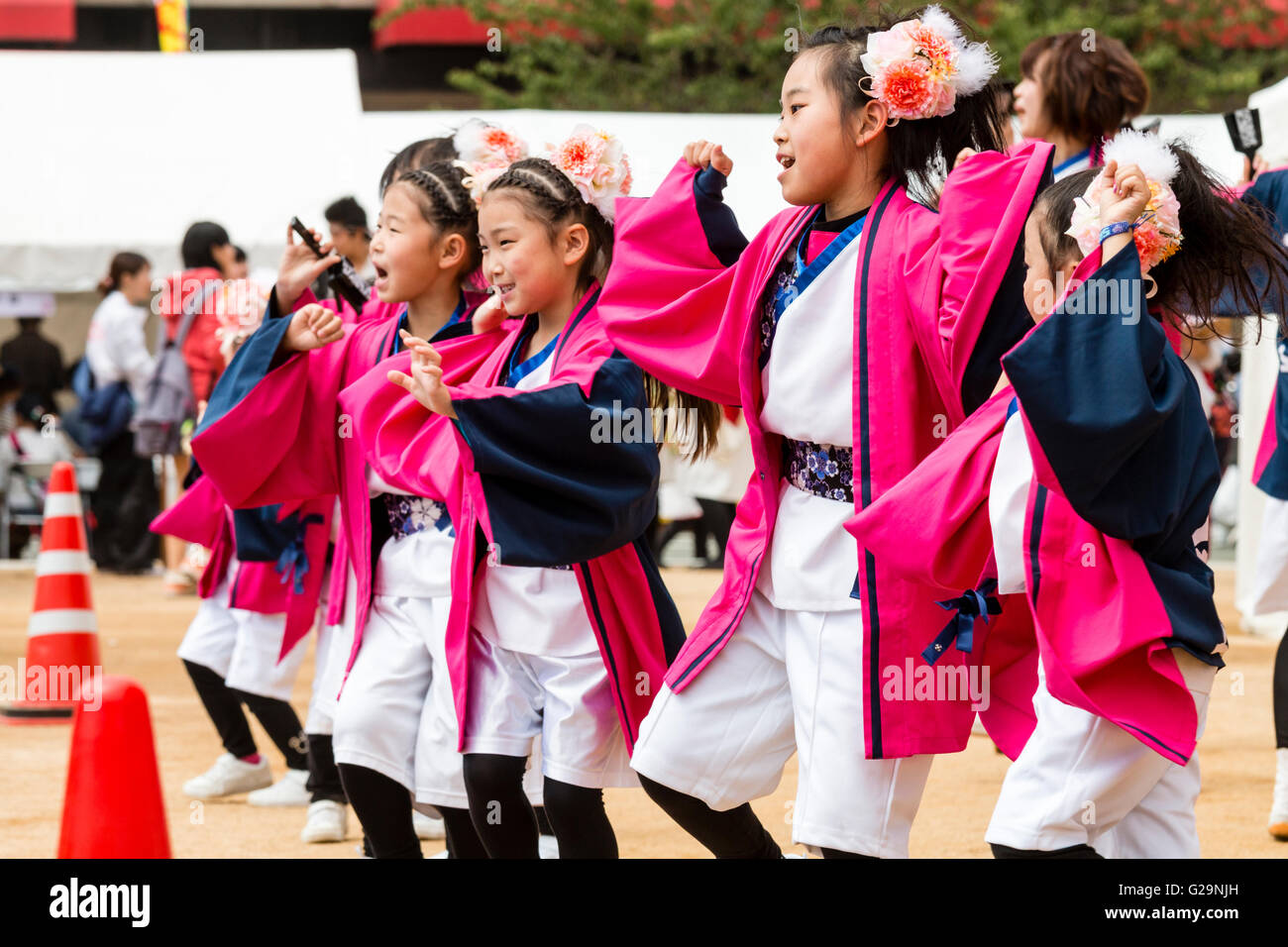 Japan, Kumamoto. Hinokuni Yosakoi dance festival. Children, with flowers in hair, in a row, part of woman's team, wearing pink happi jackets, dancing. Stock Photo