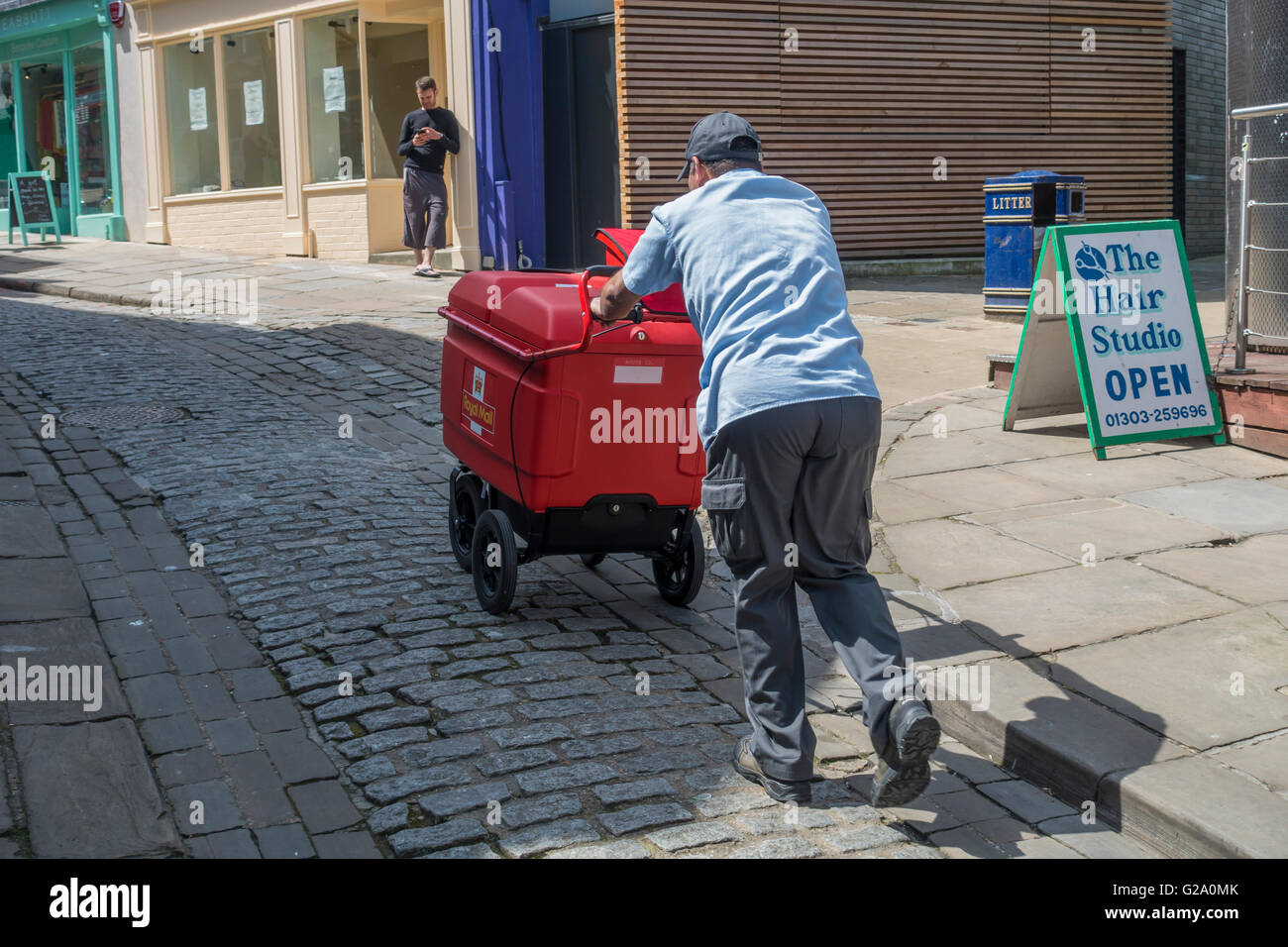 Postman Pushing Heavy Royal Mail Cart Up Hill Stock Photo
