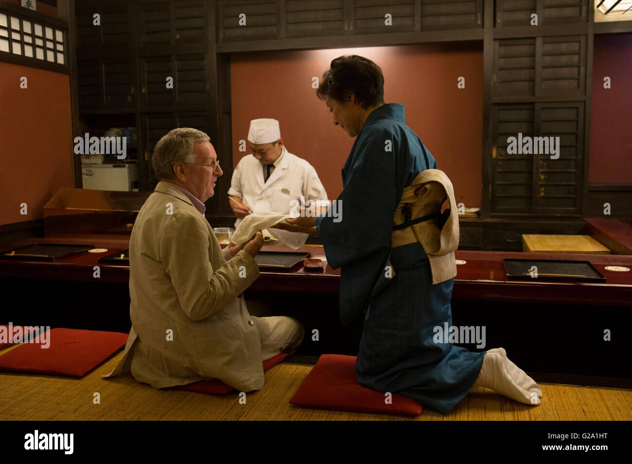 Mature Caucasian man taking hot towel from Japanese hostess Stock Photo