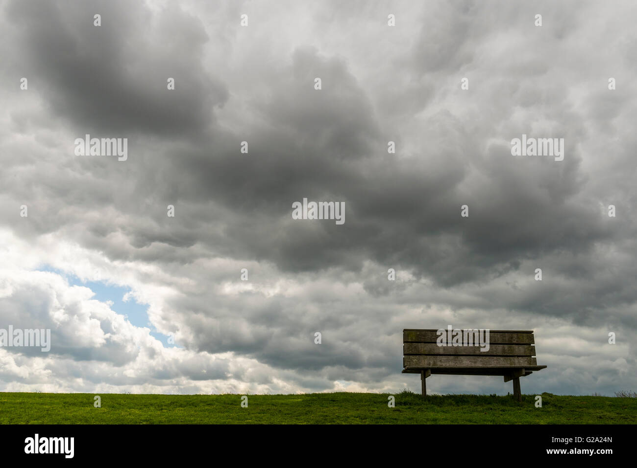 Bench on a dike in Friesland with dark rain and storm clouds. Netherlands. Stock Photo
