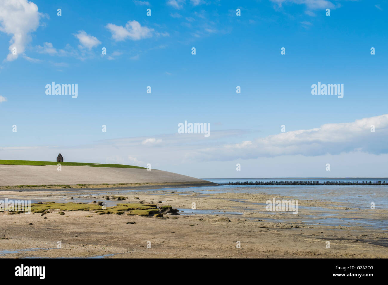 Coastline of the Waddensea at Friesland with mud flats, dike and protection poles and church of Wierum. Stock Photo