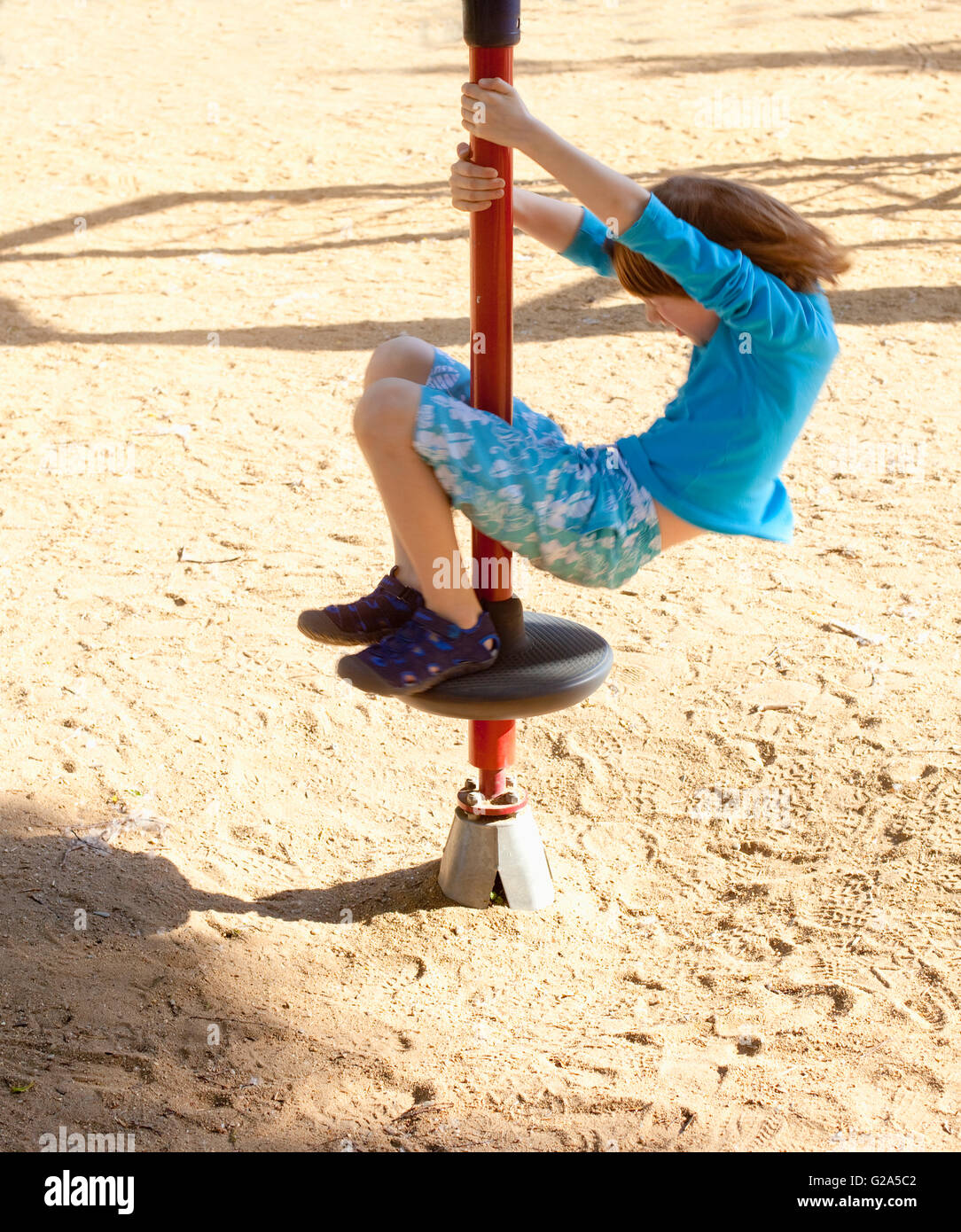 Boy with Blond Hair Spinning on a Pole at Playground Stock Photo