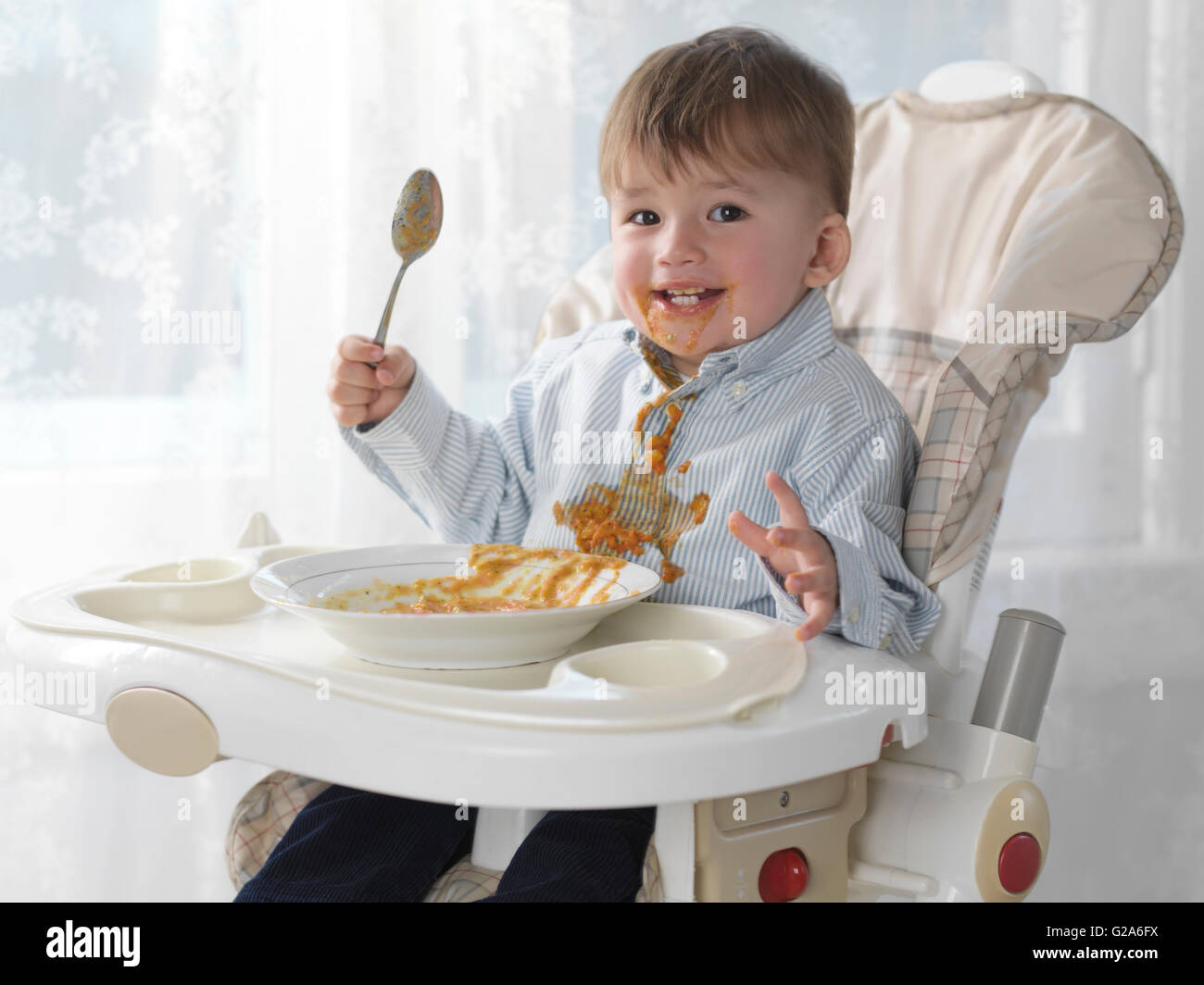Toddler Boy Sitting In A High Chair Eating Soup With A Spoon