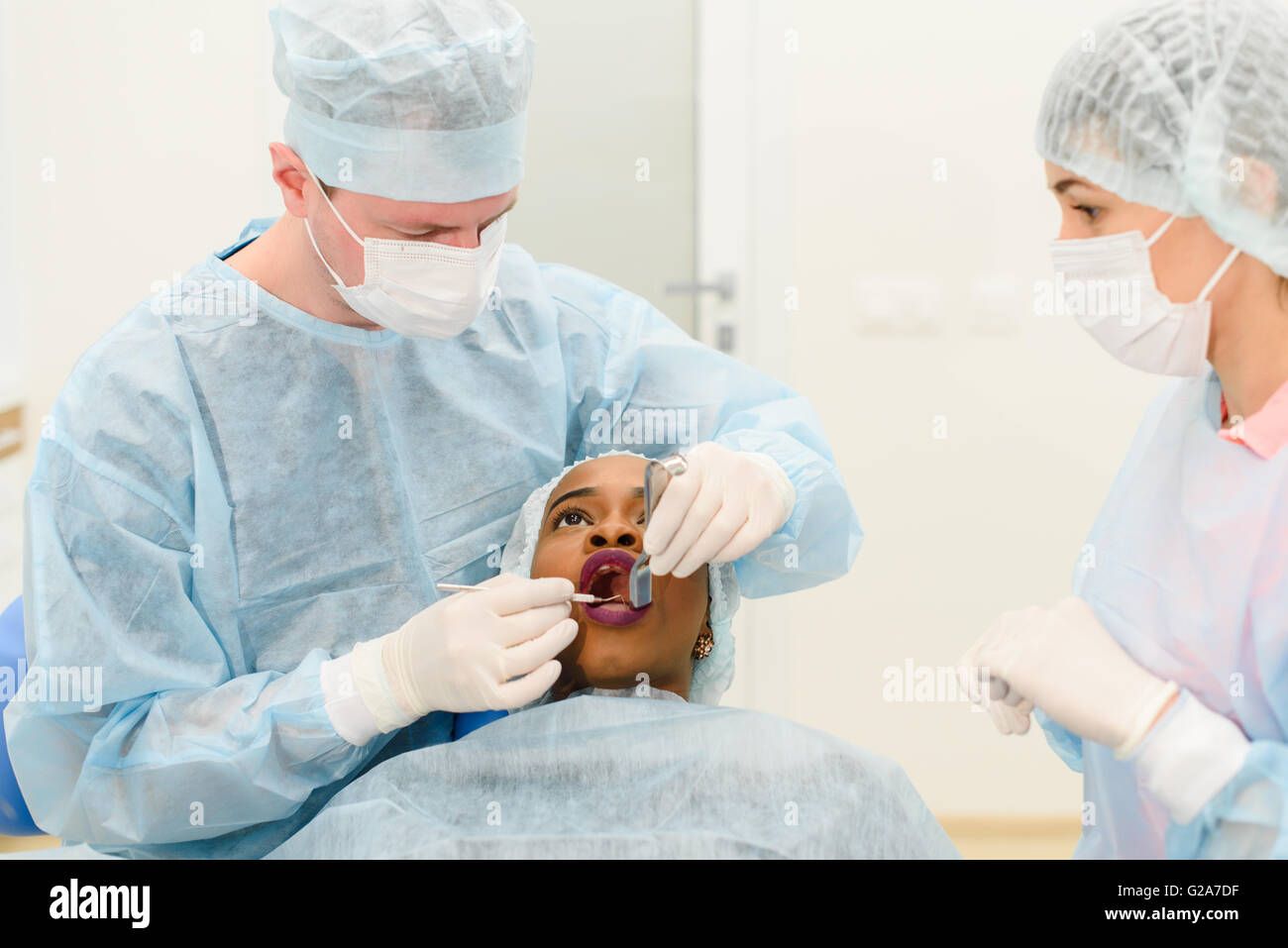 Dentist with assistant wearing uniforms making medical procedures female patient in scrup cup at