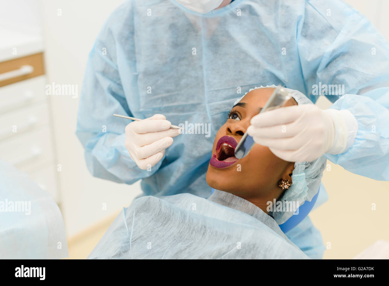 Dentist with assistant wearing uniforms making medical procedures female patient in scrup cup at