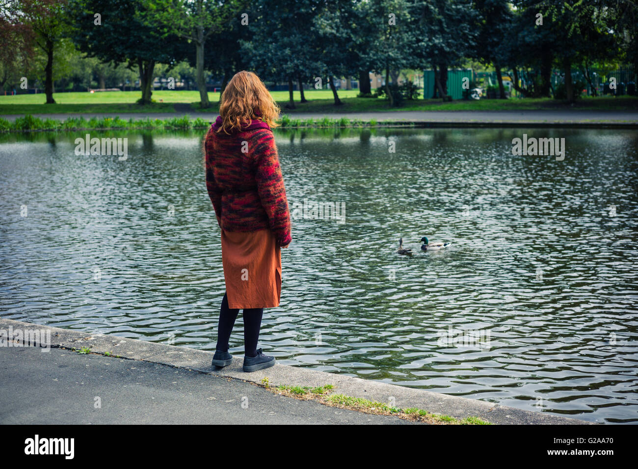 A young woman is standing by a pond in the park Stock Photo - Alamy