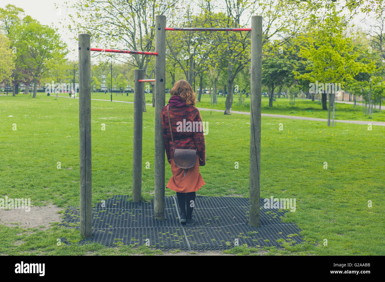 A young woman is standing in a park by some pull up bars Stock Photo
