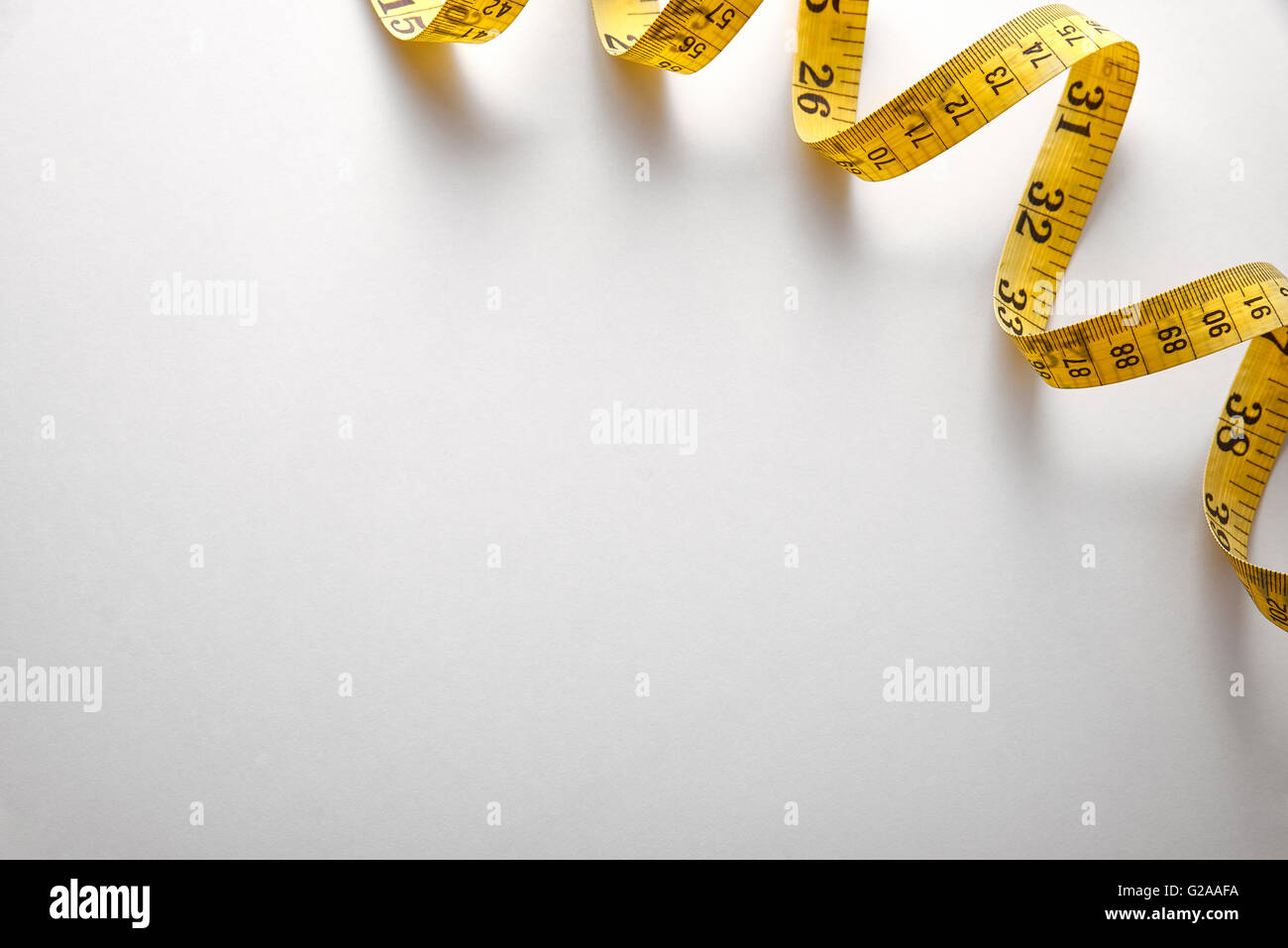 Yellow tape measure in meters and inches in a spiral on white table. Top view. Horizontal composition. Stock Photo