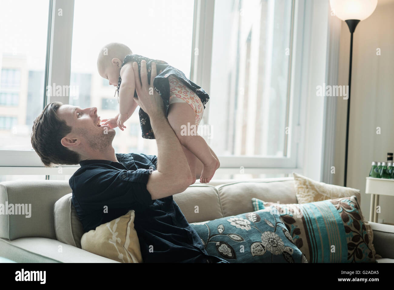 Father sitting on sofa and playing with baby daughter (2-5 months) Stock Photo