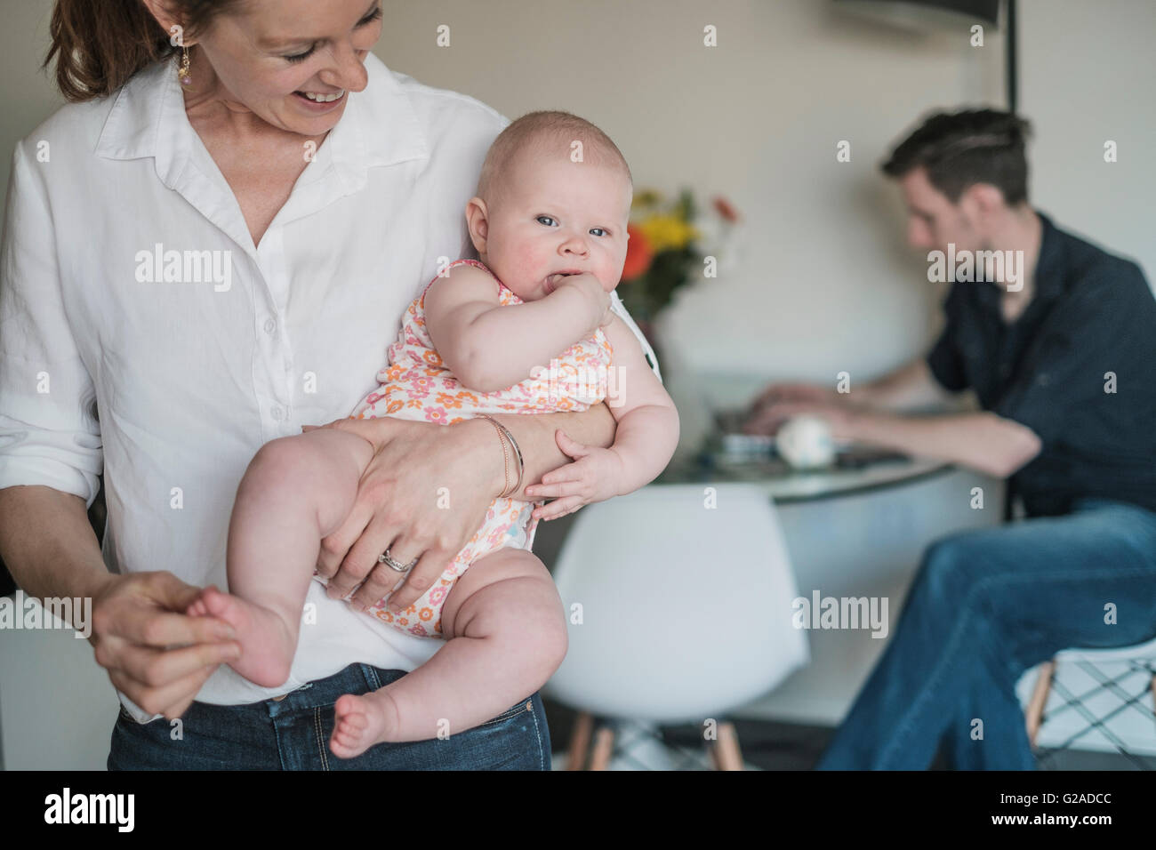 Mother holding baby (2-5 months) and father working in background Stock Photo