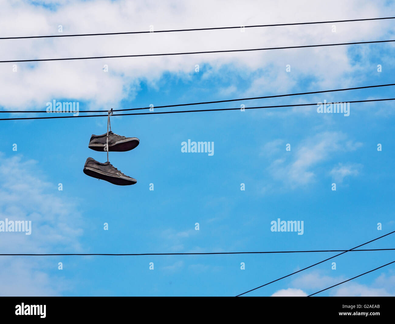 Pair of shoes hanging on cable lines against sky Stock Photo