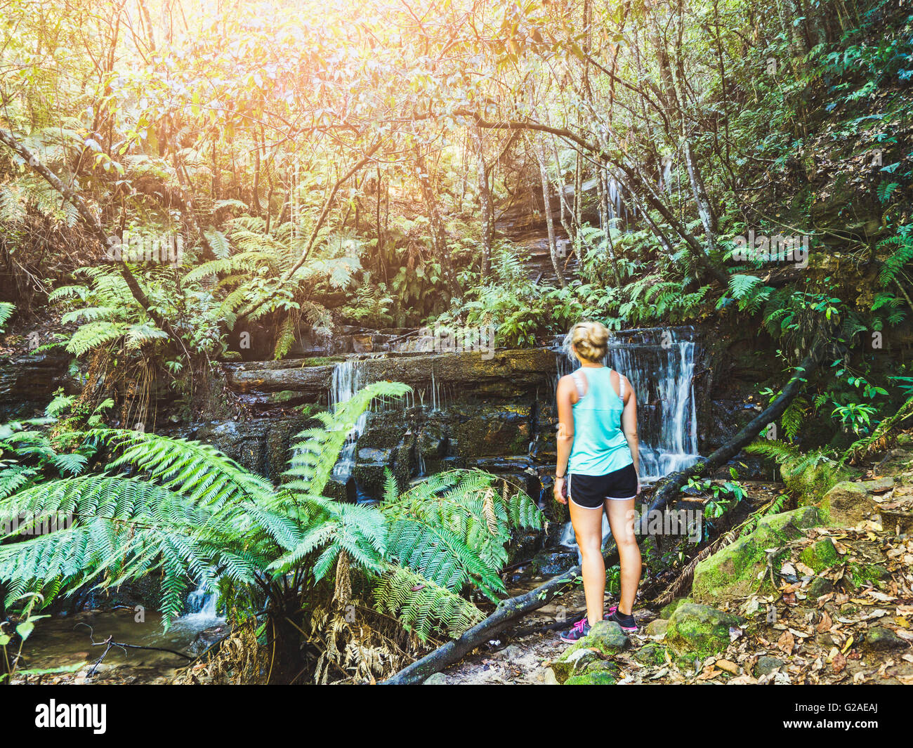 Young woman standing by waterfall in rainforest Stock Photo