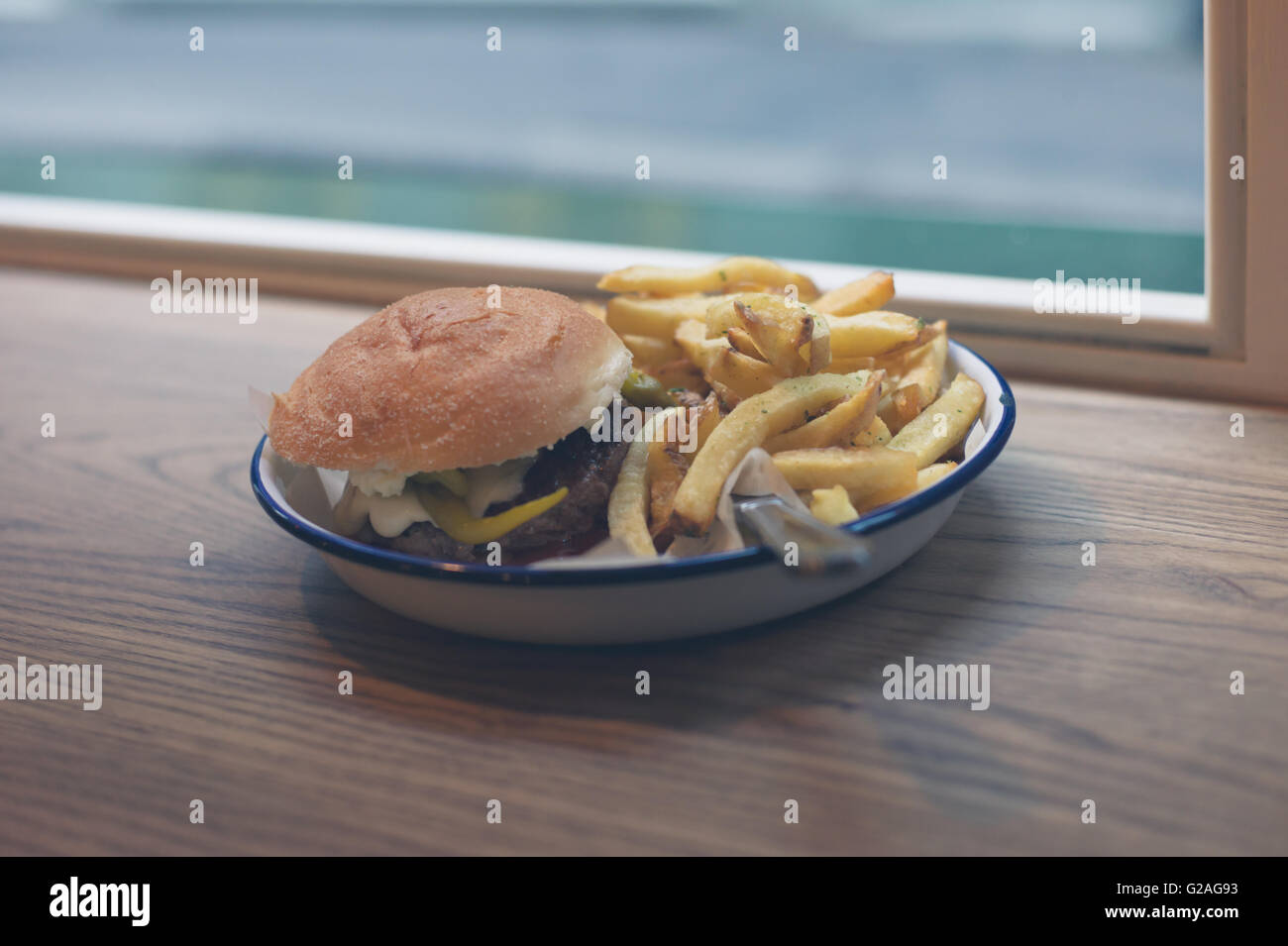 A burger and a side of fries on a plate by the window Stock Photo