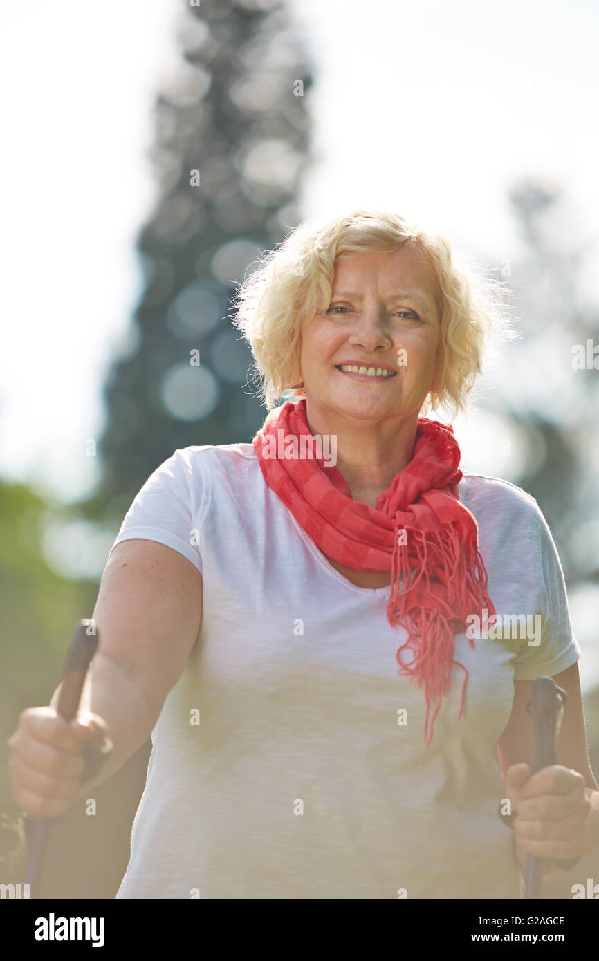 Senior woman walking with hiking sticks in summer in nature Stock Photo