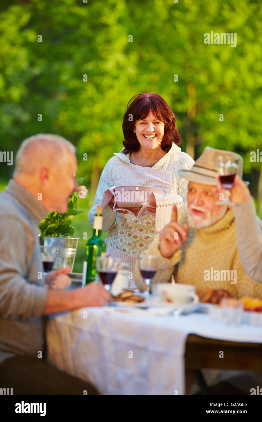 Happy senior friends celebrating birthday in a garden with cake and red wine Stock Photo