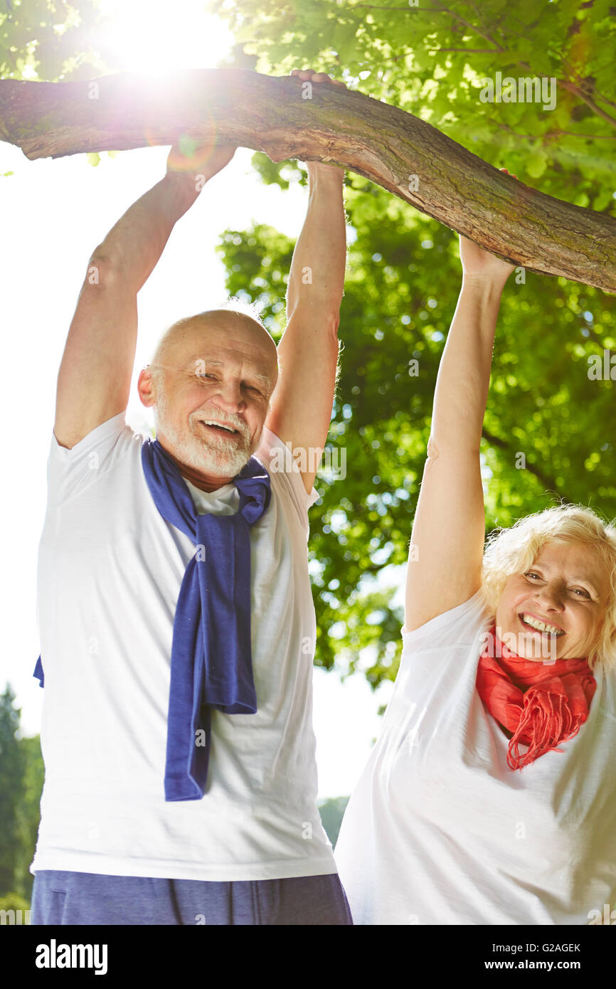 Old man and senior woman doing sports in nature hanging on a tree Stock Photo
