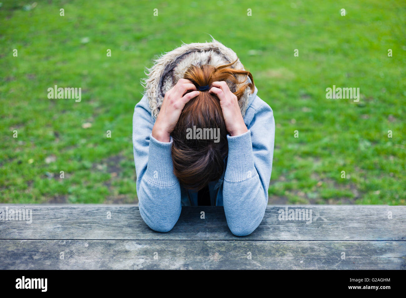 A sad young woman with her head in her hands at a table in the park Stock Photo