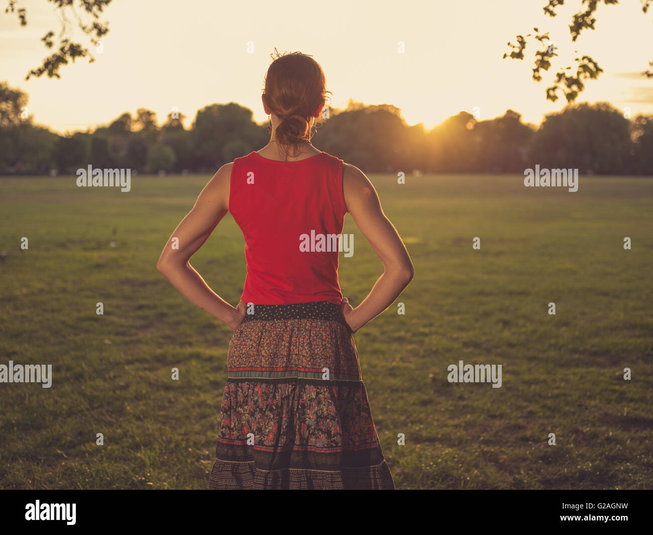 A young woman is standing in a park and is admiring the sunset Stock ...
