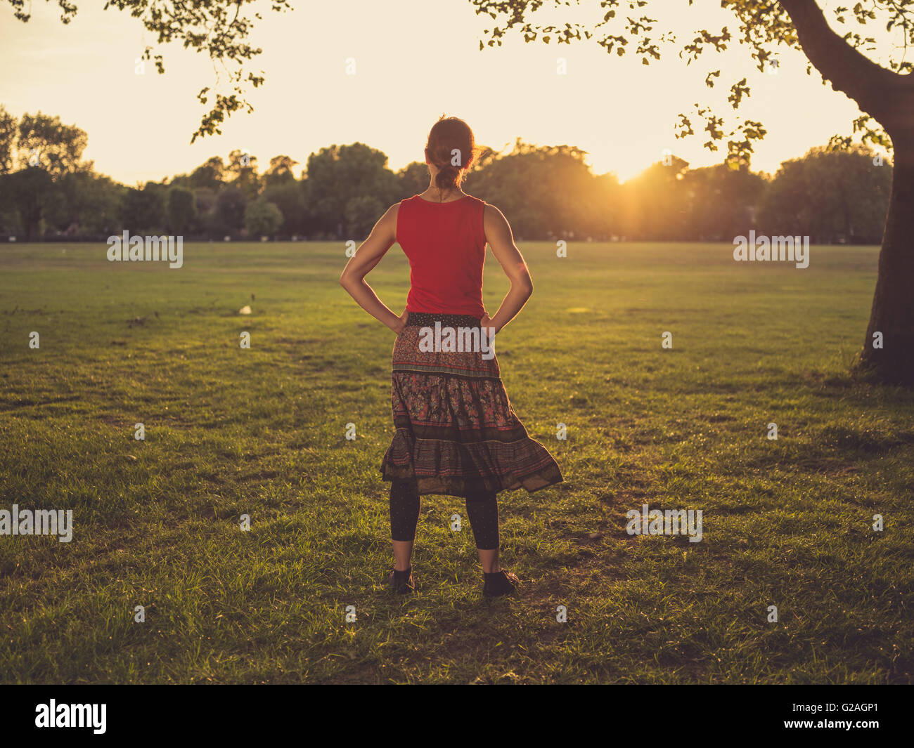 A young woman is standing in a park and is admiring the sunset Stock ...