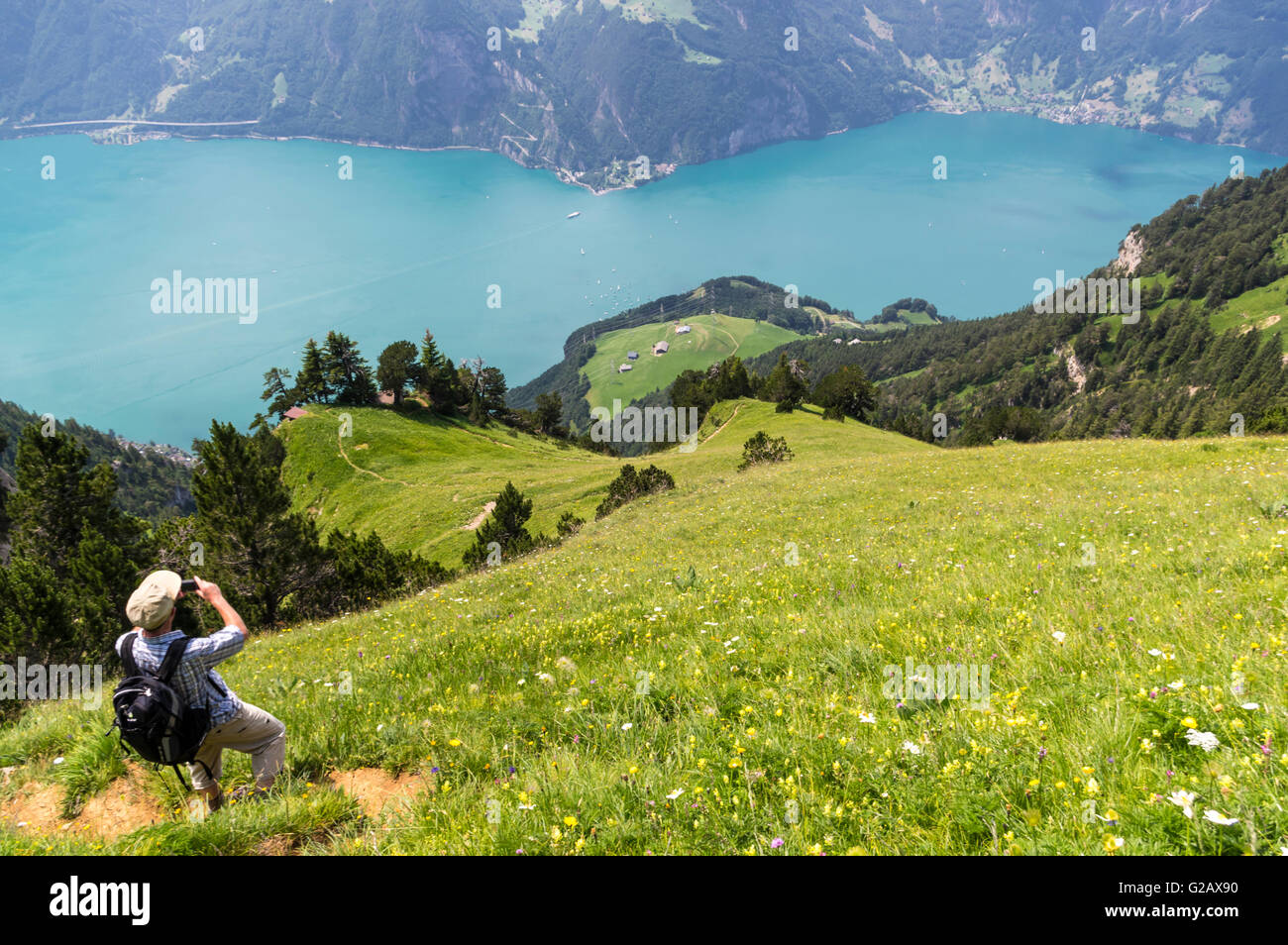 Hiker on a trail high above Lake Lucerne taking a picture of the lake and its surroundings. Canton of Uri, Central Switzerland. Stock Photo