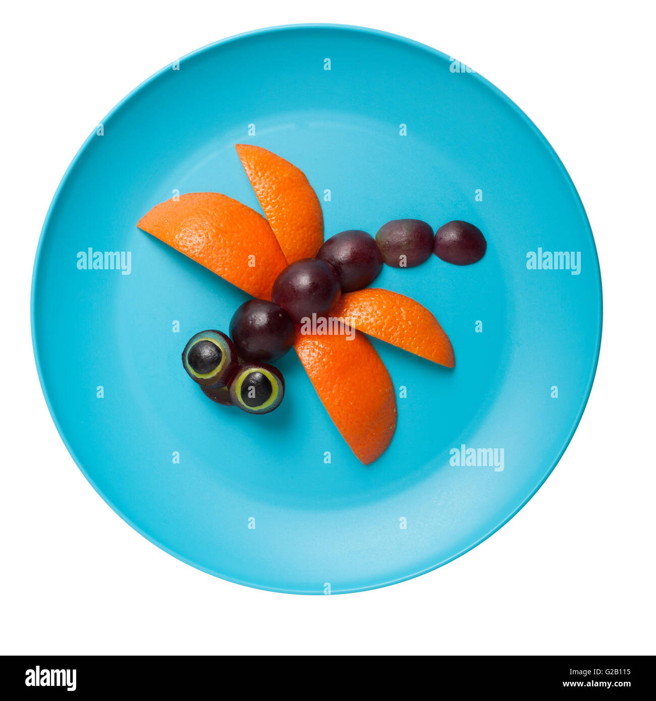Dragonfly made of orange and grape on plate Stock Photo