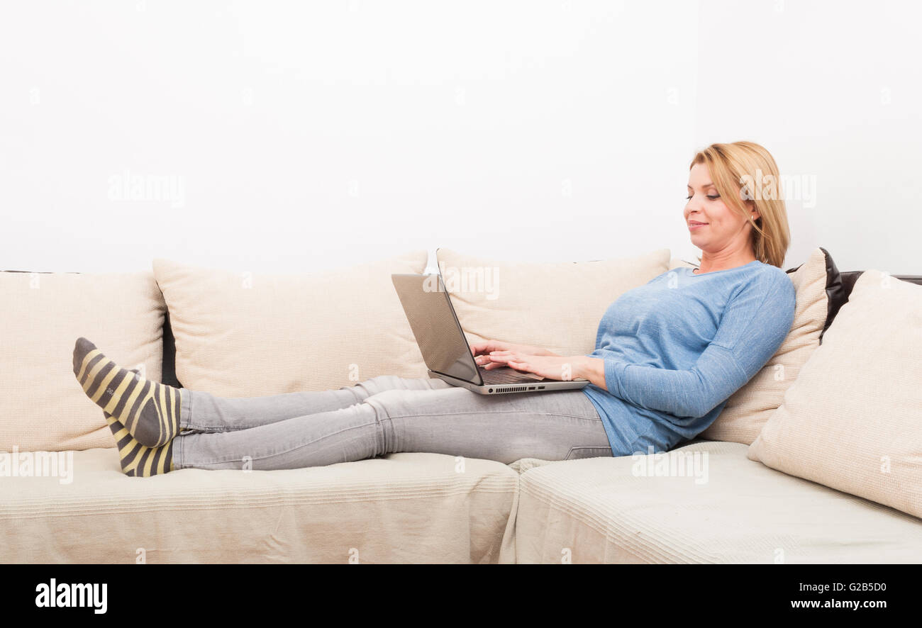 Single woman smiling and chatting online concept at home on the sofa or couch Stock Photo