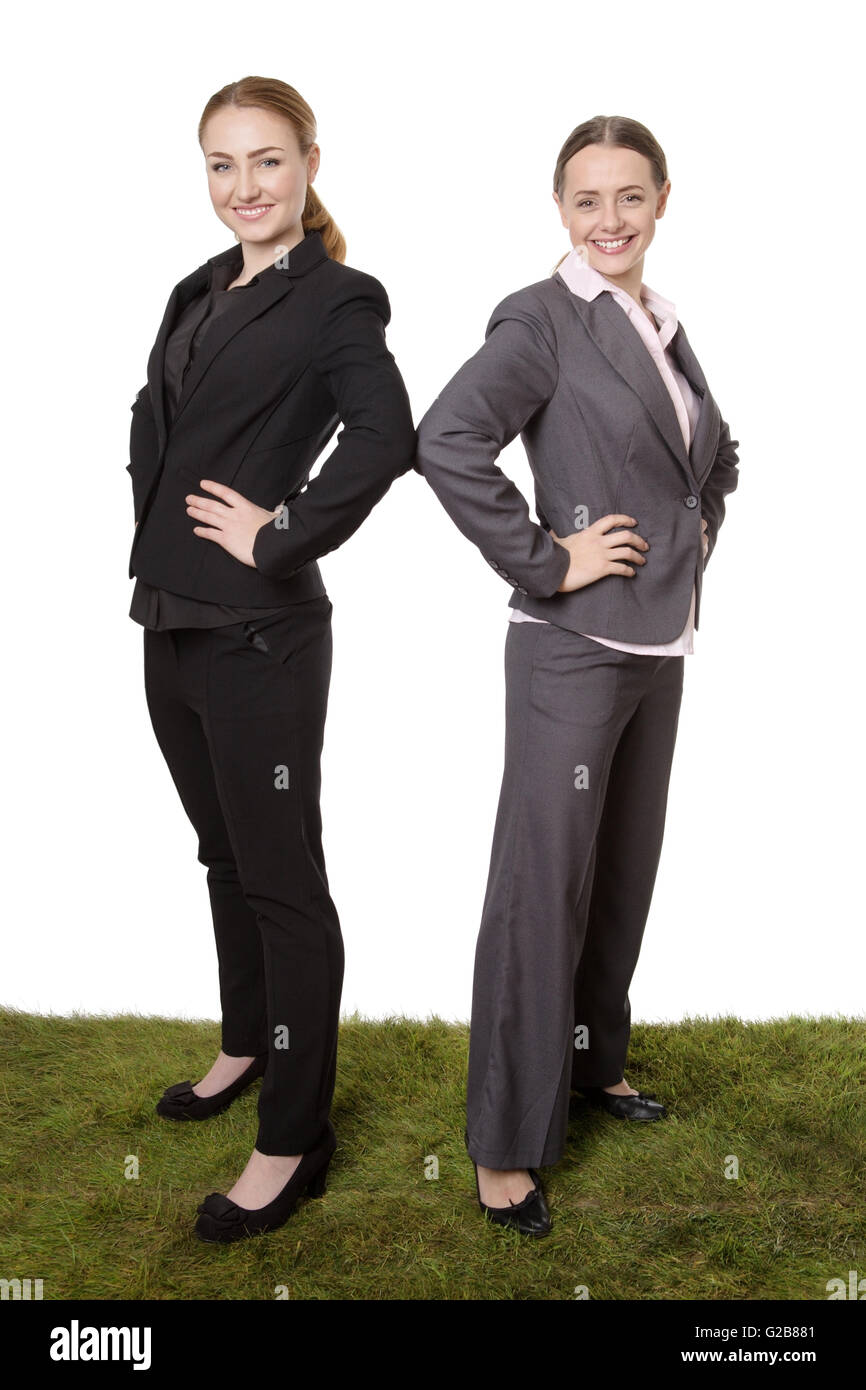 Studio shot of two Successful female business models posing with their hands on their hips, standing on grass. Stock Photo