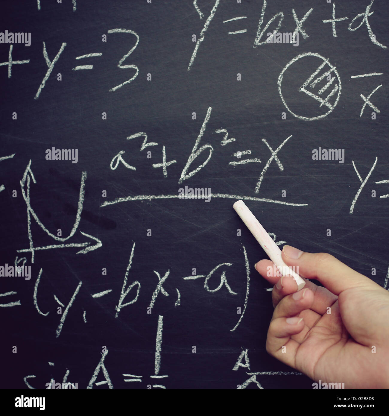 Teacher writing various high school maths formula on chalkboard. Stock Photo