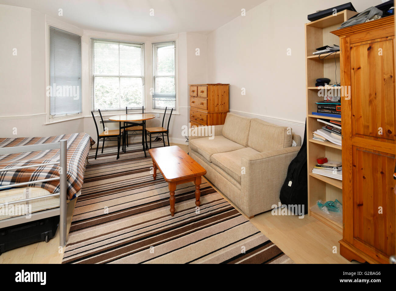 Inglewood Road, West Hampstead. View of a studio apartment with dining table in front of windows and a small sofa. Stock Photo