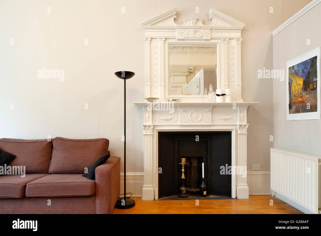 Pembridge Square, Notting Hill. View of a traditional fireplace with a mirror above it. Partial view of a couch. Picture hanging on the wall above wall radiator. Stock Photo