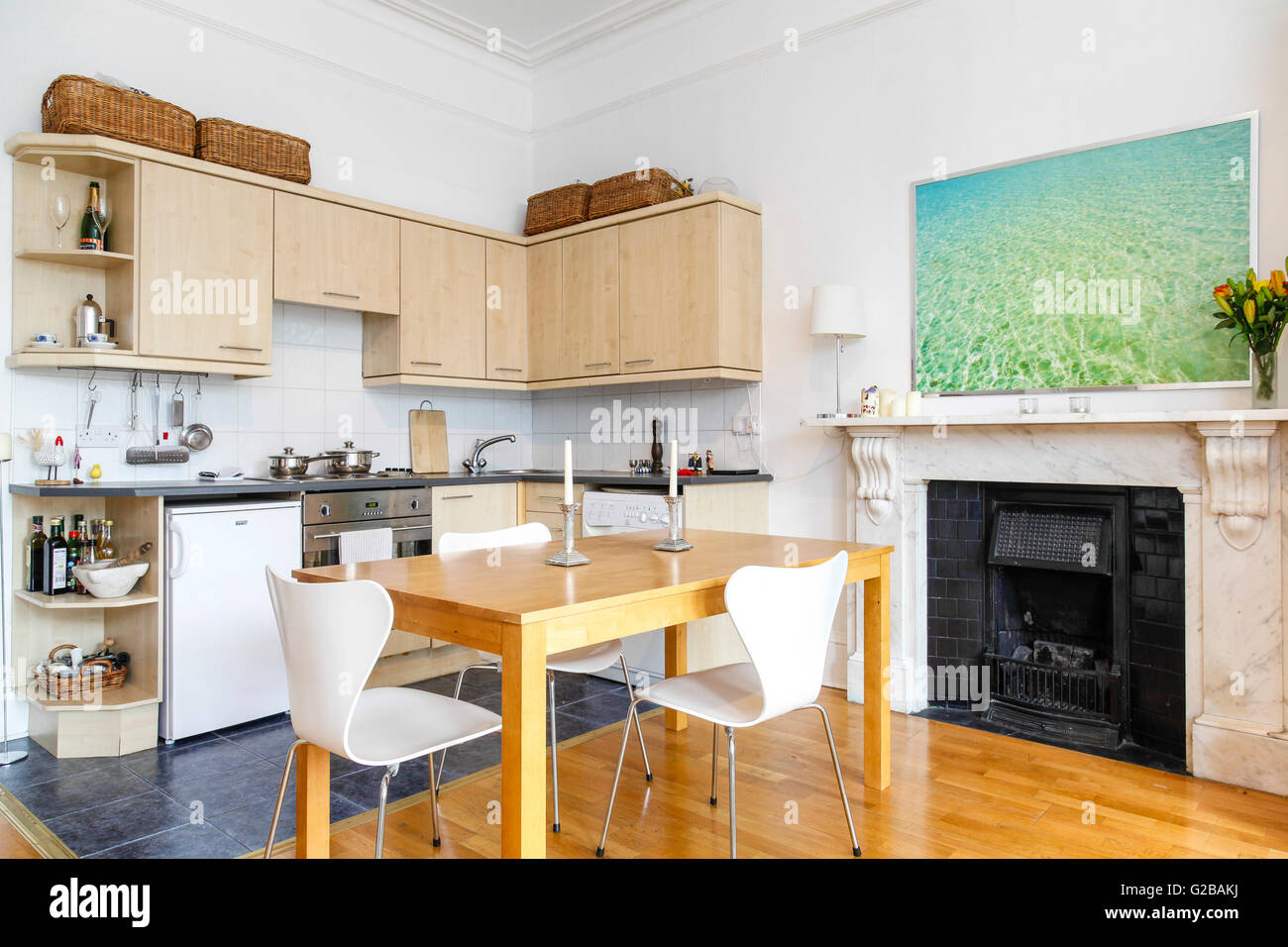 Pembridge Square, Notting Hill. View of a contemporary kitchen and dining area. Wood table and white chairs on top of wood floor. Picture hanging above fireplace. Stock Photo