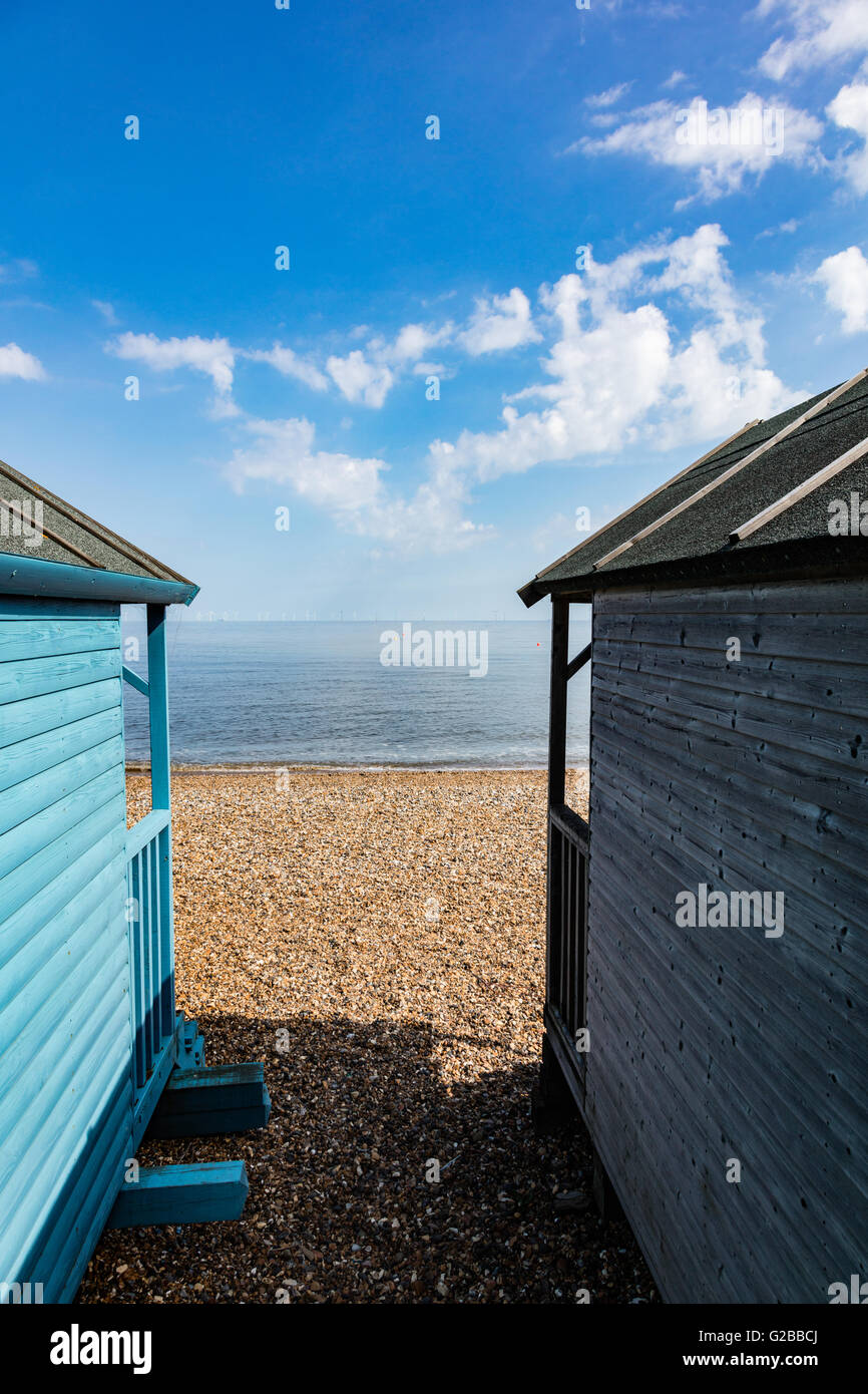 View between beach huts of the Thames Estuary and windfarm on the horizon, Hampton, Herne Bay, Kent, UK Stock Photo