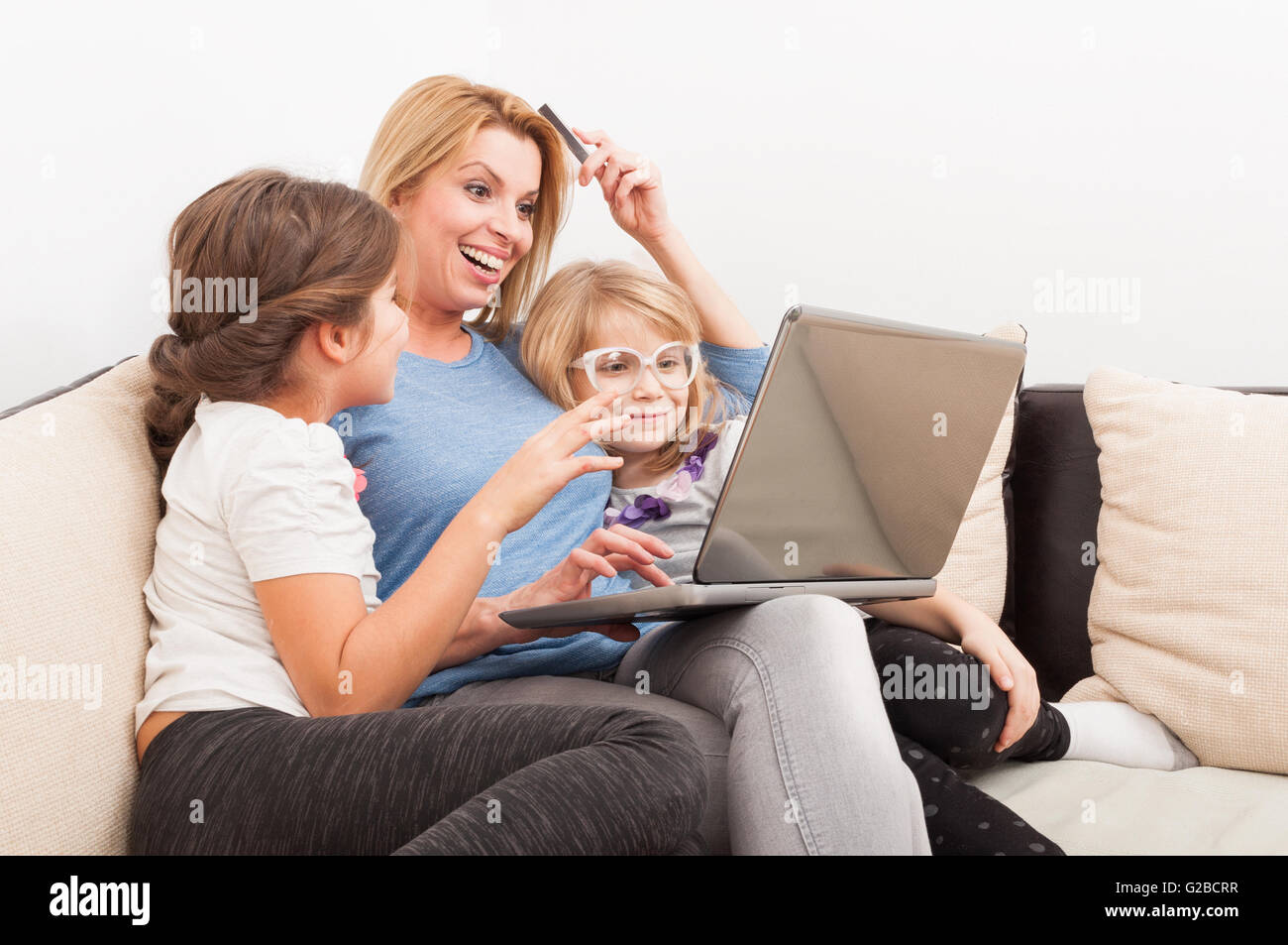 Mother and daughters shopping online using laptop smiling on the couch or sofa Stock Photo