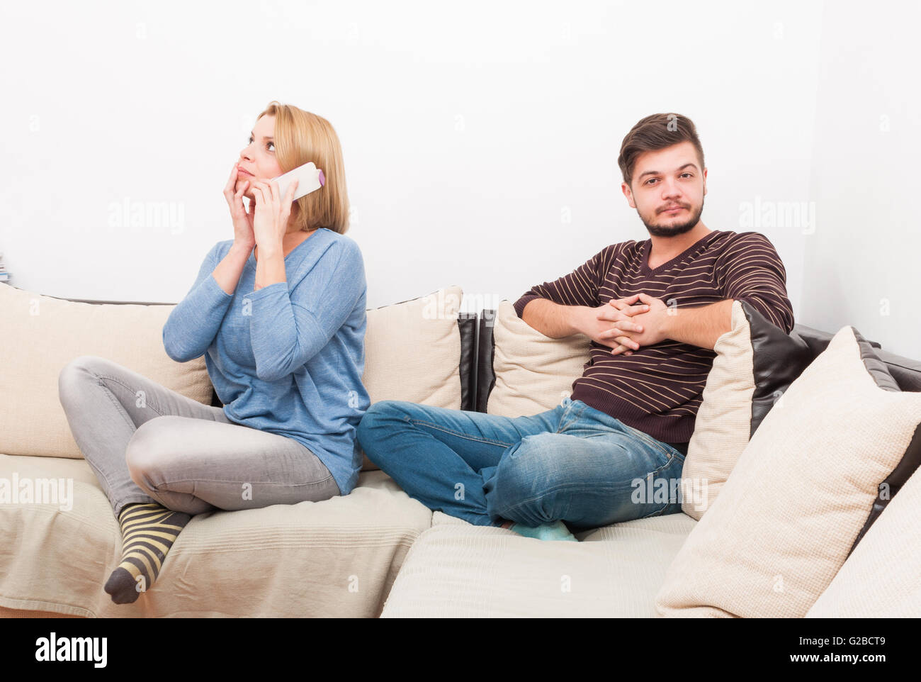 Cheating wife talking privately on the phone while husband waits on the sofa Stock Photo