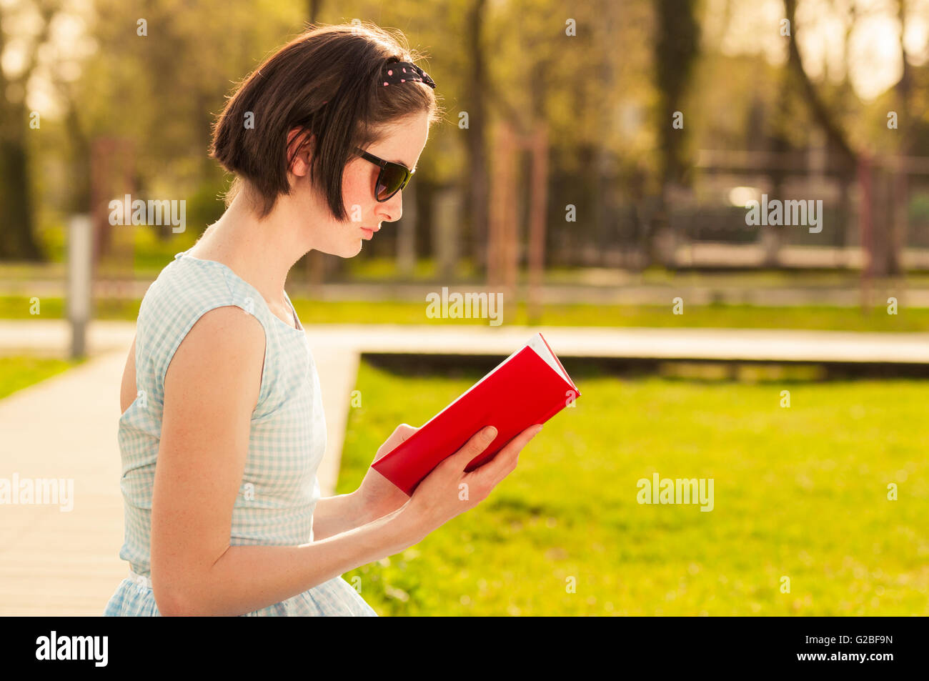 Beautiful young woman sitting in the park and reading a book as ...