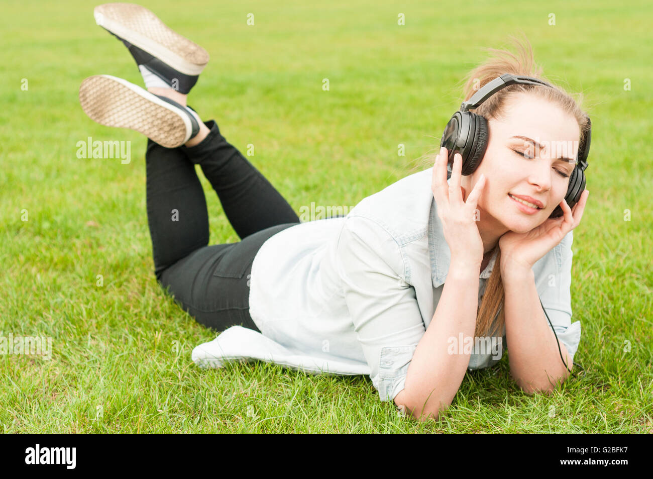 Young woman relaxing outdoor lying on grass and listen to music in a ...