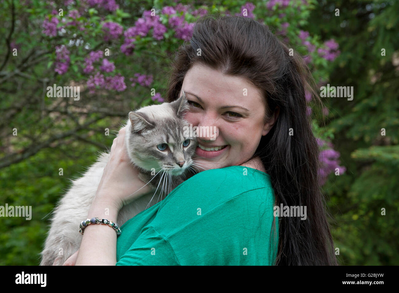 Woman smiles as she snuggles Siamese mix cat Stock Photo