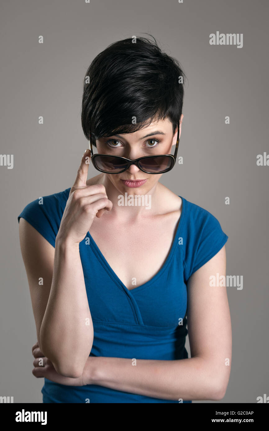 Young short hair brunette beauty peeking at camera above sunglasses over  gray studio background Stock Photo - Alamy