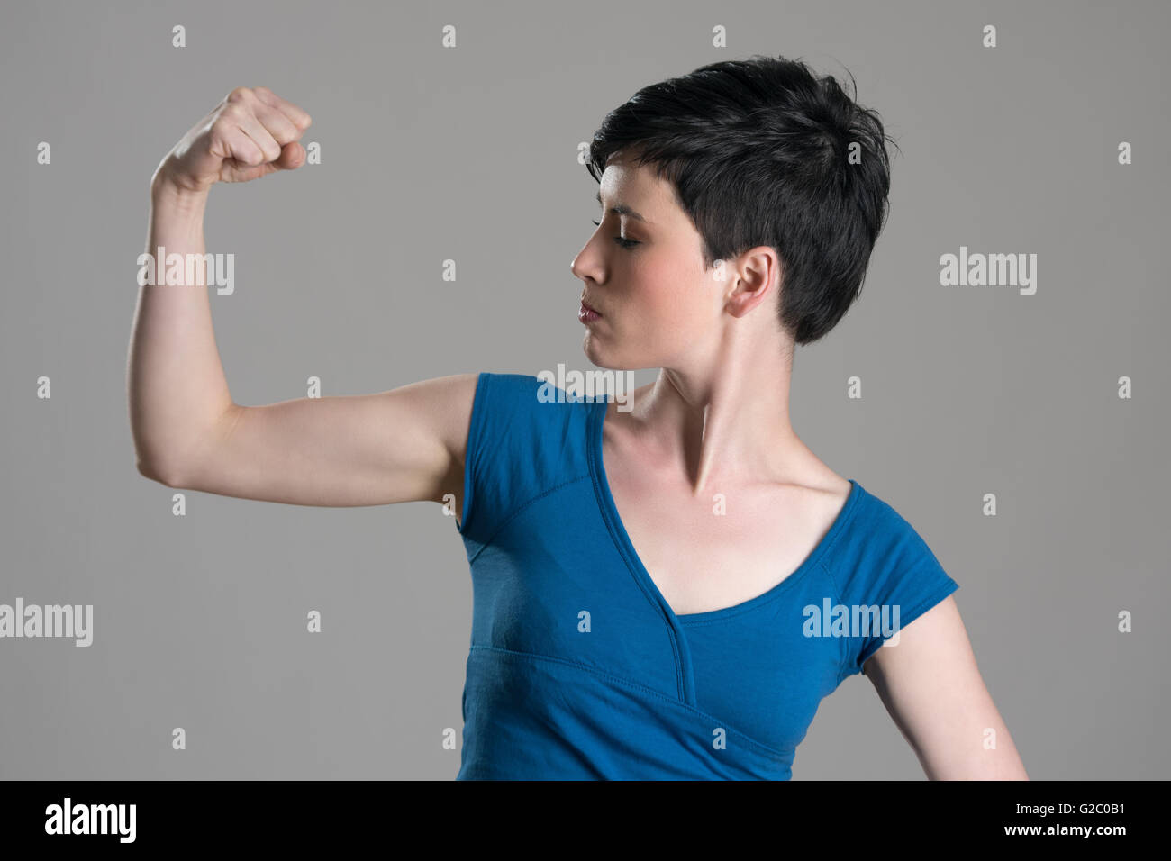 Slim young short hair woman flexing arm bicep muscle over gray studio background. Stock Photo