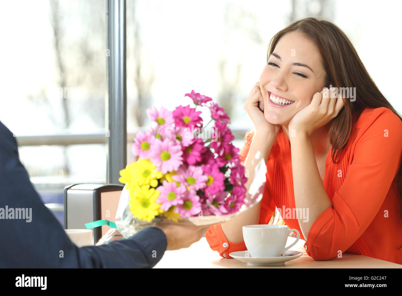 Couple dating and boyfriend giving a bouquet of flowers to his candid girlfriend in a coffee shop Stock Photo