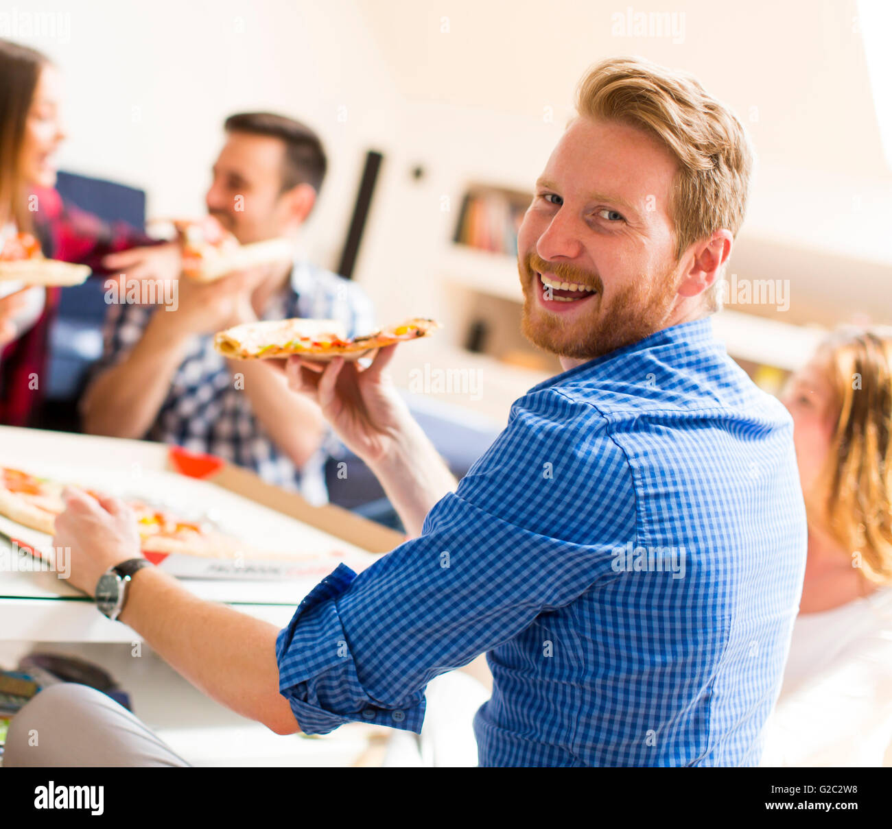 Group of happy young people eating pizza in the room Stock Photo