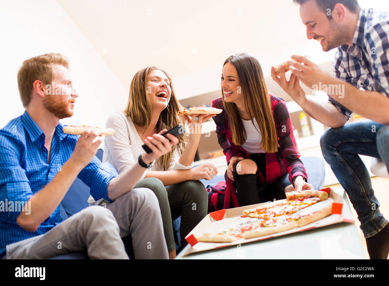 Group of happy young people eating pizza in the room Stock Photo