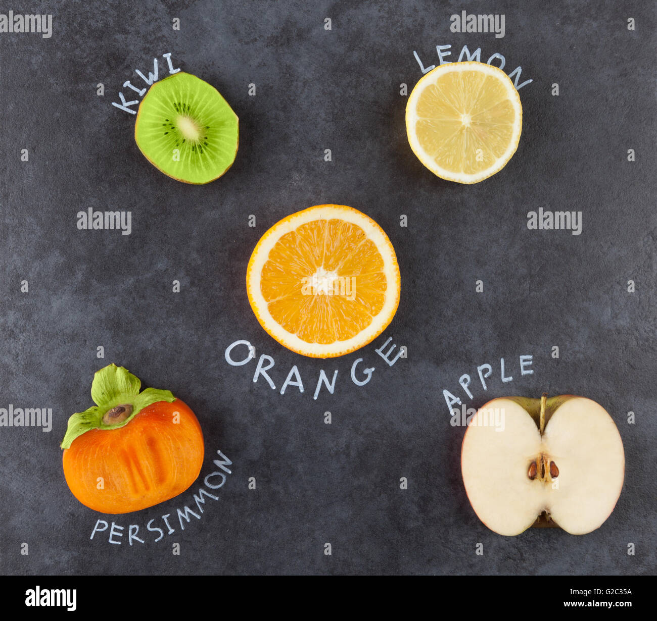 Slices of fruit on grungy dark background. Kiwi, lemon, orange, persimmon, apple. Top view. Stock Photo