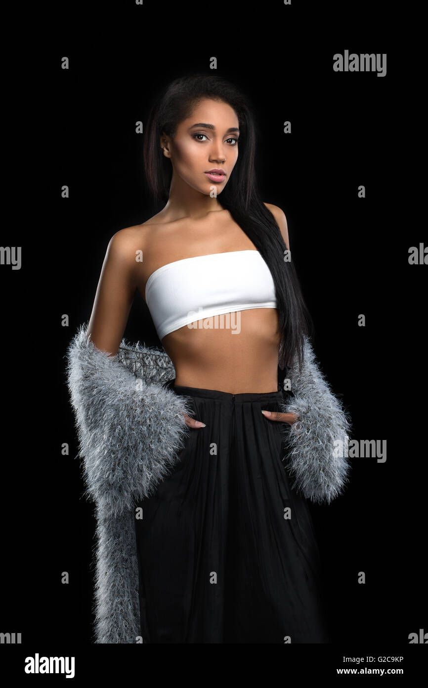 Handsome mulatto woman with long hairstyle fashion posing in fur cape on dark background. African american girl looking at camera. Stock Photo