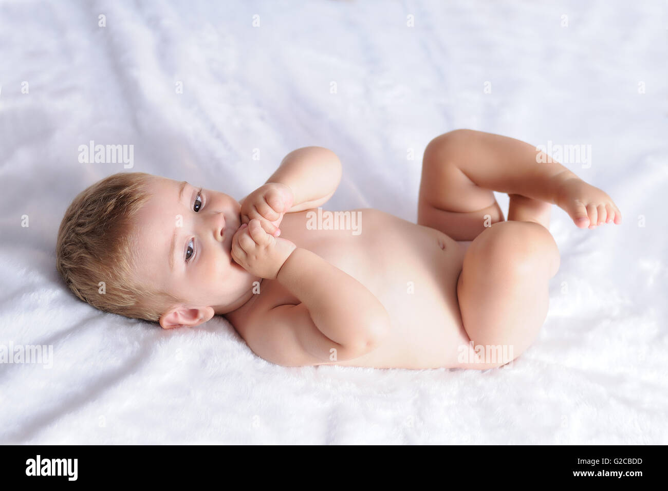Baby Biting Hands Lying On A Blanket Of White Hair Stock Photo