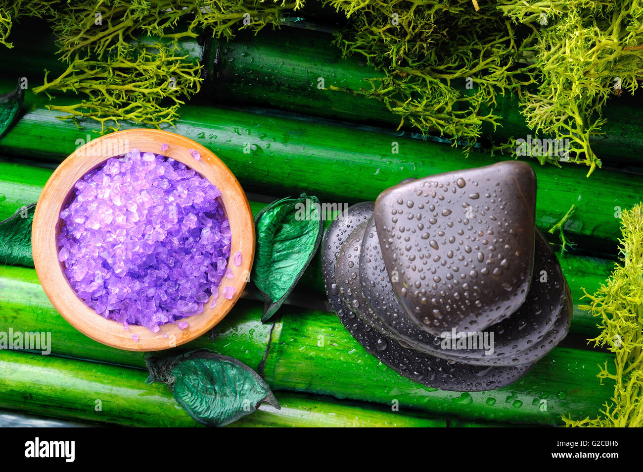 Stack of black stones and salt for massage and bath surrounded by moss on bamboo. Concept of massage and alternative medicines. Stock Photo