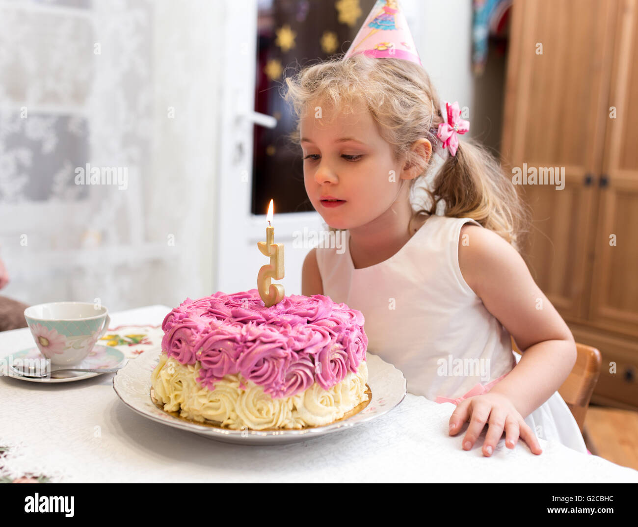Portrait of little pretty girl with 5 year birthday cake, sitting at table and make a wish Stock Photo