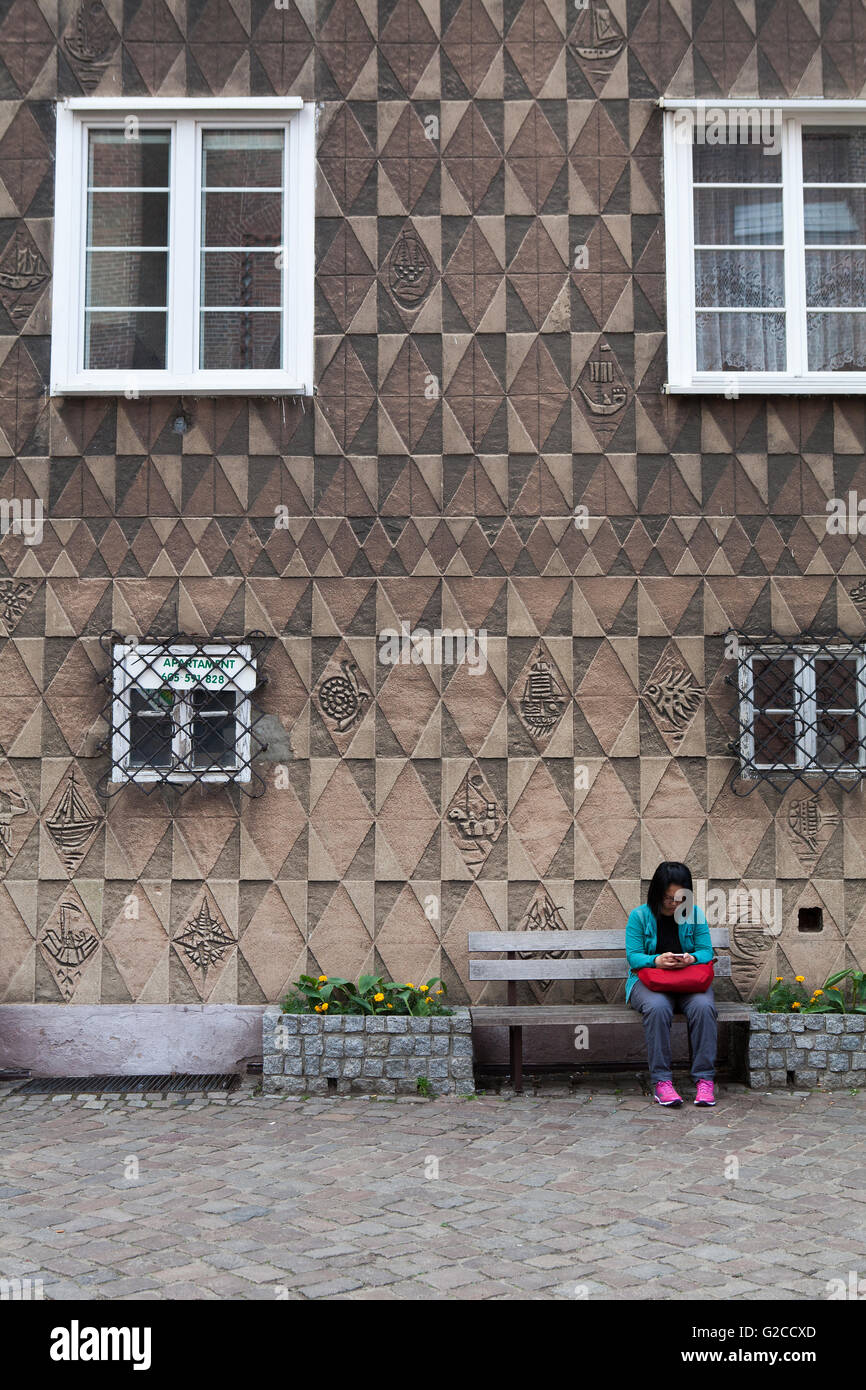 A woman sits and checks her phone in front of a Sgraffito house, Stock Photo
