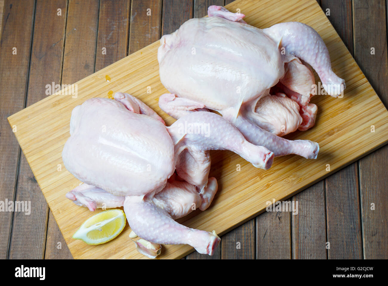 Whole raw Chicken on rustic wooden board and garlic, lemon Stock Photo